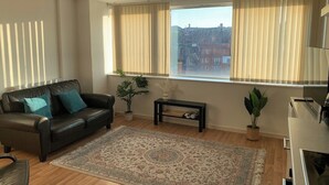 A living room with a leather sofa, a coffee table, a rug, and a large window with curtains. - Cosy Apartment with great Wi-Fi, City Centre (Nottingham)