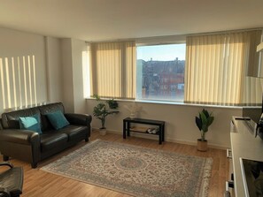 Ein Wohnzimmer mit einem Ledersofa, einem Couchtisch, einem Teppich und einem großen Fenster mit Vorhängen.