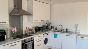 A compact kitchen with a microwave, toaster, sink, and a washing machine. - Cosy Apartment with great Wi-Fi, City Centre (Nottingham)