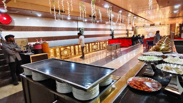 A buffet setup with a counter, food trays, and a seating area with tables and chairs. - HOTEL DREAM PALACE (Basai)