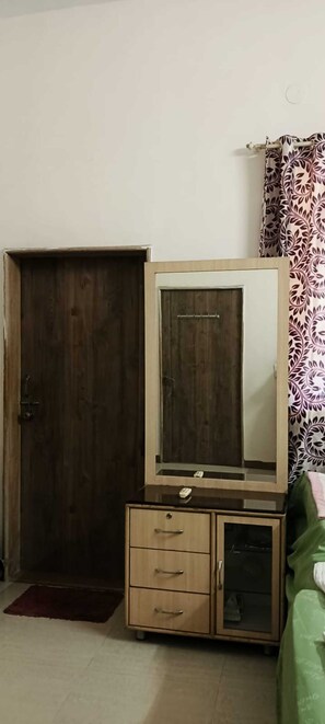 Une pièce comprenant une armoire en bois, un meuble avec miroir et un lit recouvert d’une couverture verte.