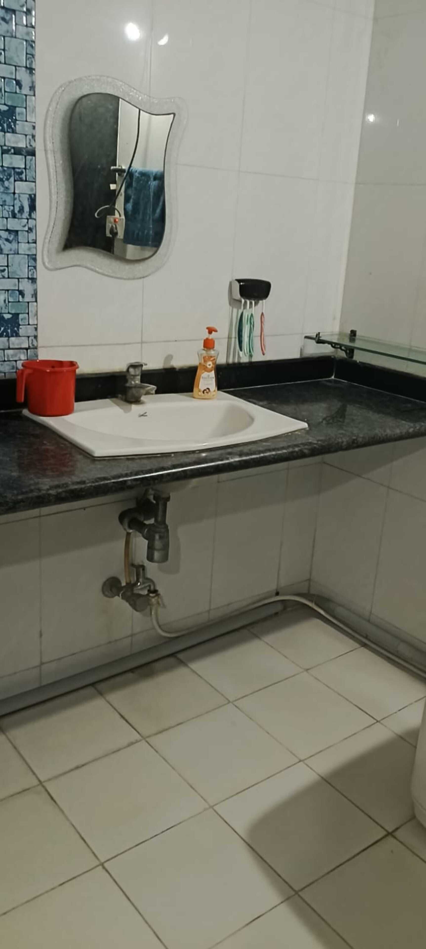 A bathroom with a white sink, a mirror, a red cup, and a bottle of hand soap.