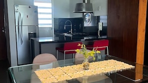 Une cuisine moderne avec une table à manger en verre, des chaises et un fauteuil rouge.