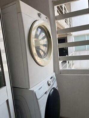 Eine gestapelte Samsung Waschmaschine und ein Trockner mit Frontlader in einem Hauswirtschaftsraum, mit Fenster und Metallgeländer.