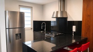 Une cuisine moderne équipée d’un réfrigérateur en acier inoxydable, d’une cuisinière à gaz et de tabourets de bar rouges.