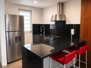 Eine moderne Küche mit einem Edelstahlkühlschrank, einem Gasherd und roten Barhocker.