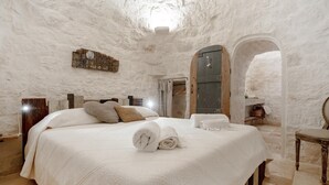 Ein Schlafzimmer mit einem großen Bett, einem hölzernen Kopfteil, einem Spiegel und einer Steinwand.