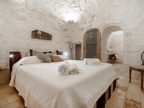 Ein Schlafzimmer mit einem großen Bett, einem hölzernen Kopfteil, einem Spiegel und einer Steinwand.