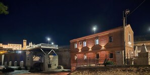 A nighttime view of a historic building with a brick facade, a stone bridge in the background, and a well-lit street.