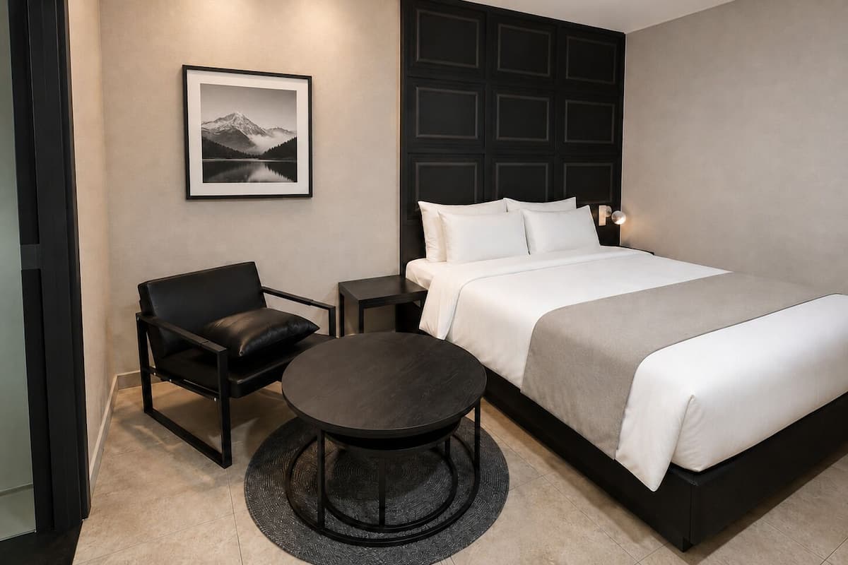 Un dormitorio moderno con cama, una silla, una mesita y un cuadro en la pared.