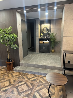 Un lobby moderno con un mostrador de recepción, una planta en maceta, una mesita y un piso de baldosas.