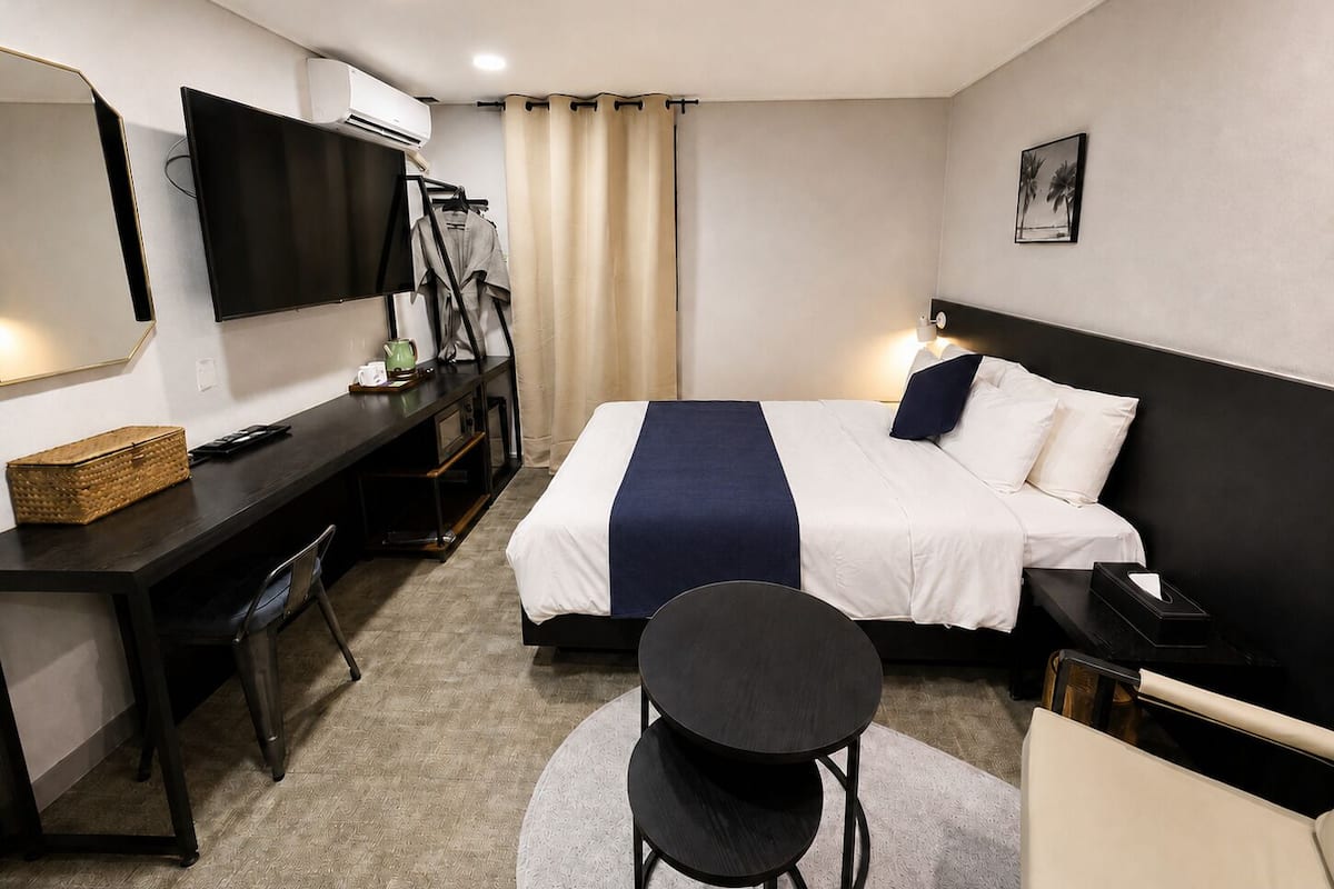 Habitación de hotel con cama, escritorio, silla, televisor y una mesita.