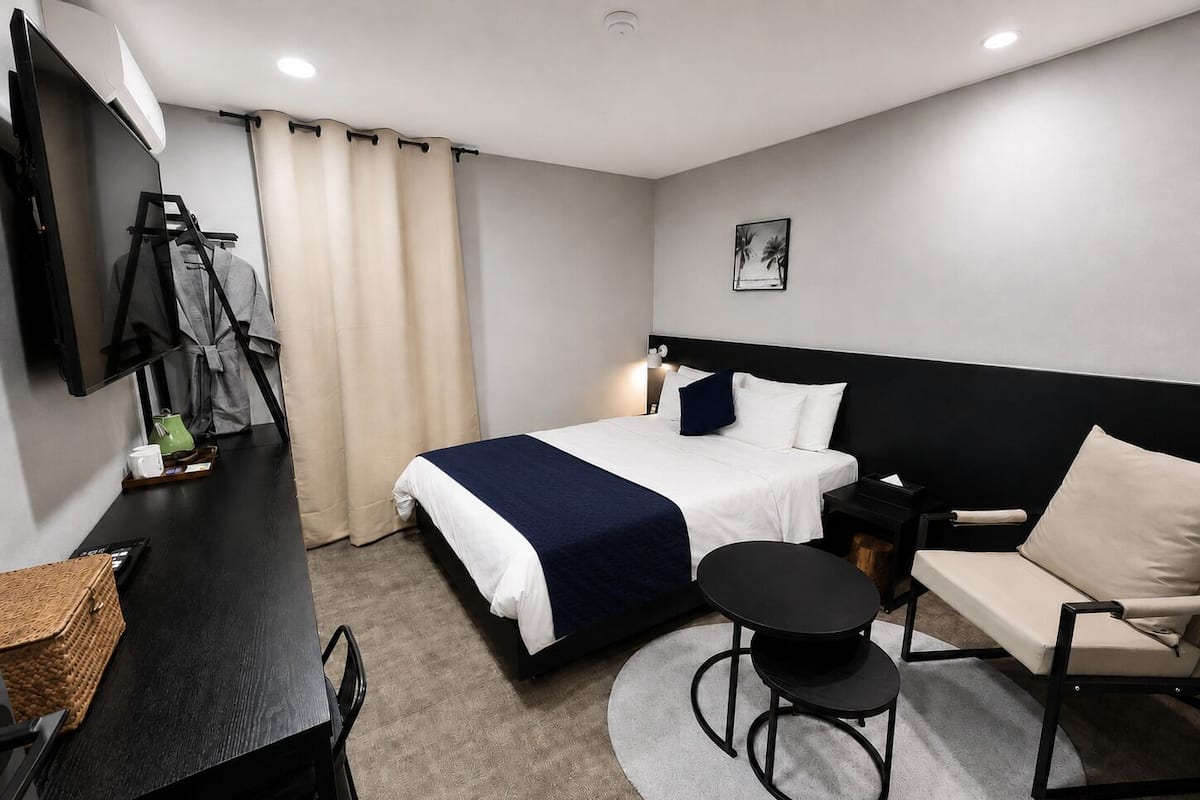Una habitación de hotel con cama, escritorio, silla, mesita y televisor.