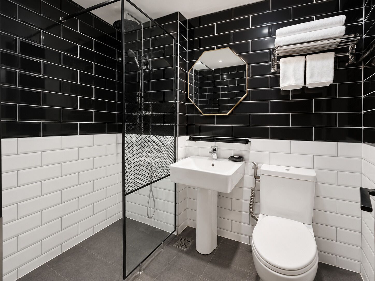 A modern bathroom with black and white tiles, a glass shower enclosure, a white sink, and a toilet.