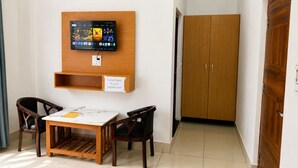 A room with a wooden TV mounted on the wall, a reception sign, a wooden table with chairs, and a wooden wardrobe.