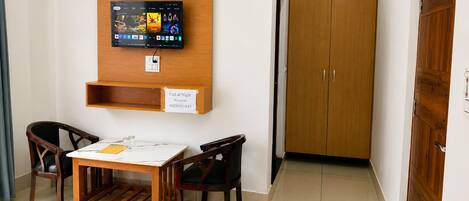 A room with a wooden TV mounted on the wall, a reception sign, a wooden table with chairs, and a wooden wardrobe.