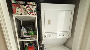 Ett kompakt tvättrum med en inbyggd tvättmaskin och torktumlare, hyllor för förvaring av rengöringsmedel och ett litet förvaringsutrymme.