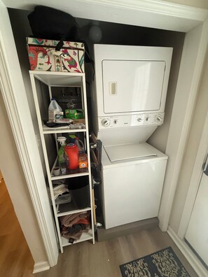 A compact laundry room with a built-in washer and dryer, shelves with cleaning supplies, and a small storage area. - Charming 2-Bedroom House - 1 mile from Mercedes Benz Stadium (Atlanta)