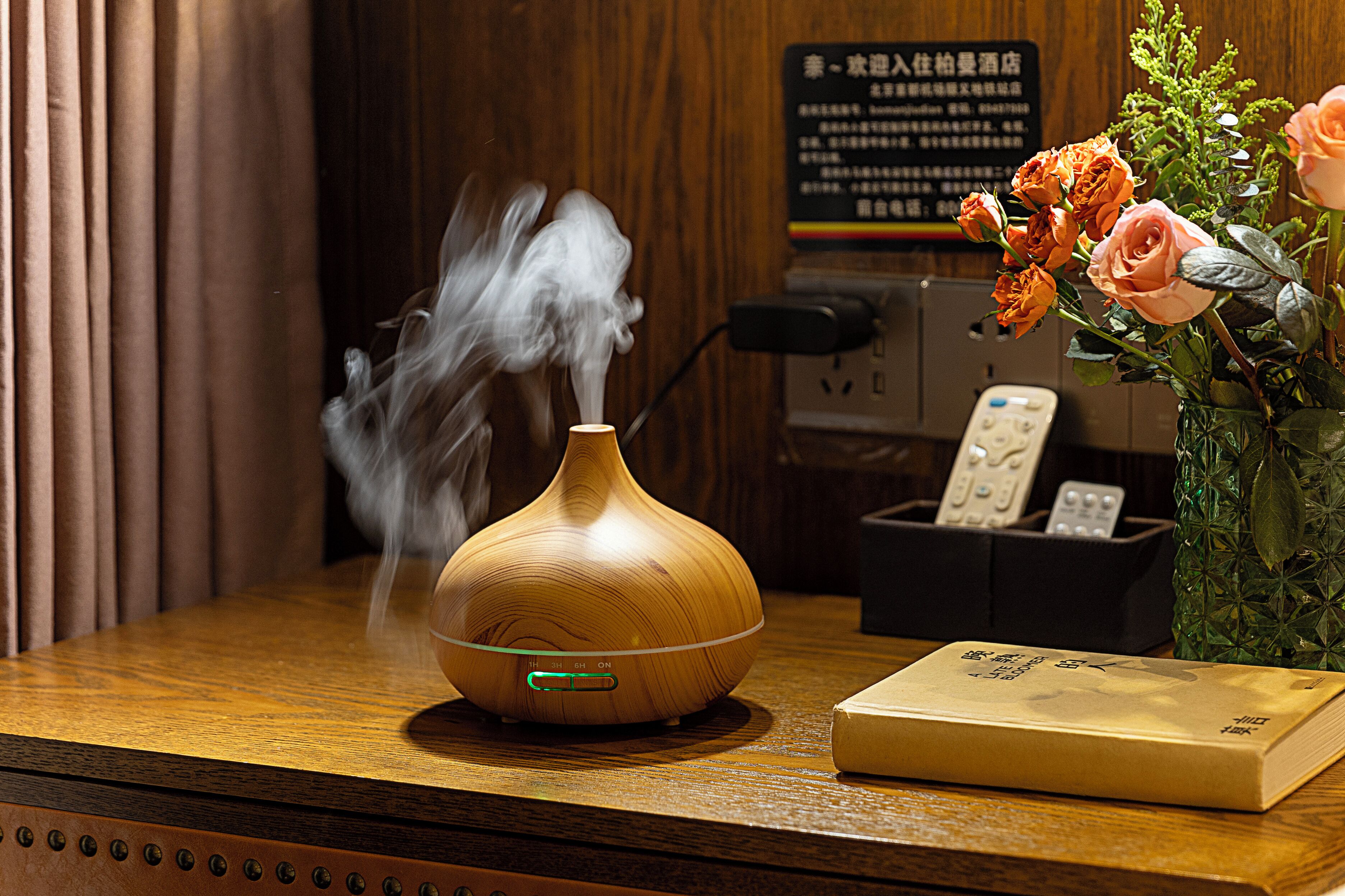 Un difusor de madera que emite vapor, un florero con flores y un control remoto sobre una superficie de madera.