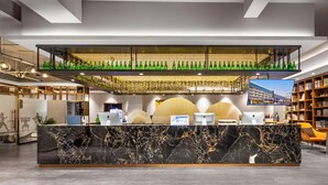 A modern hotel lobby with a marble reception desk, a lower bar area with green bottles, a large flat-screen TV, and a bookshelf. - Borrman International Hotel Shunyi (Shunyi)