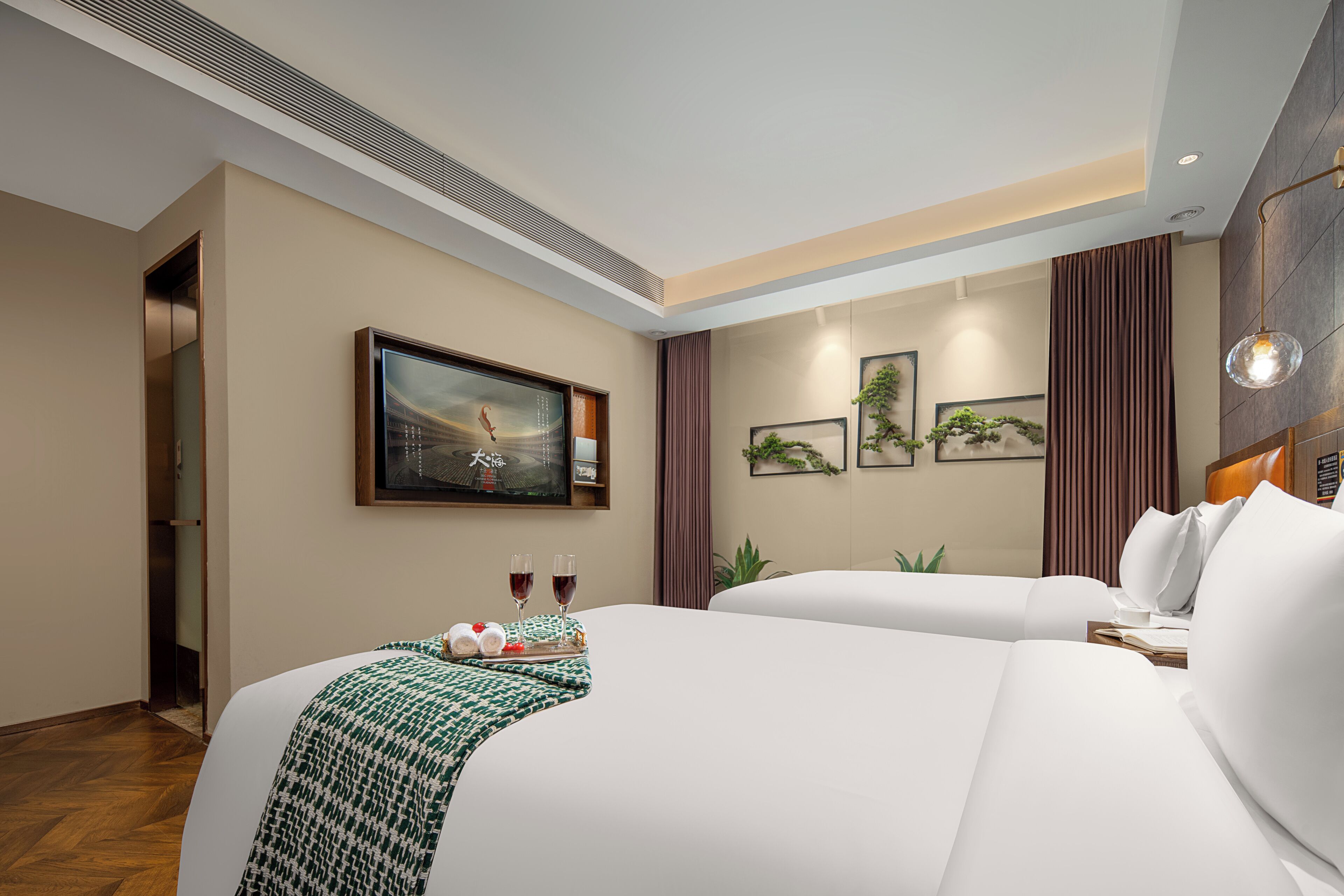 A hotel room with two beds, a painting on the wall, a tray with glasses and a fruit basket, and a plant on the windowsill.