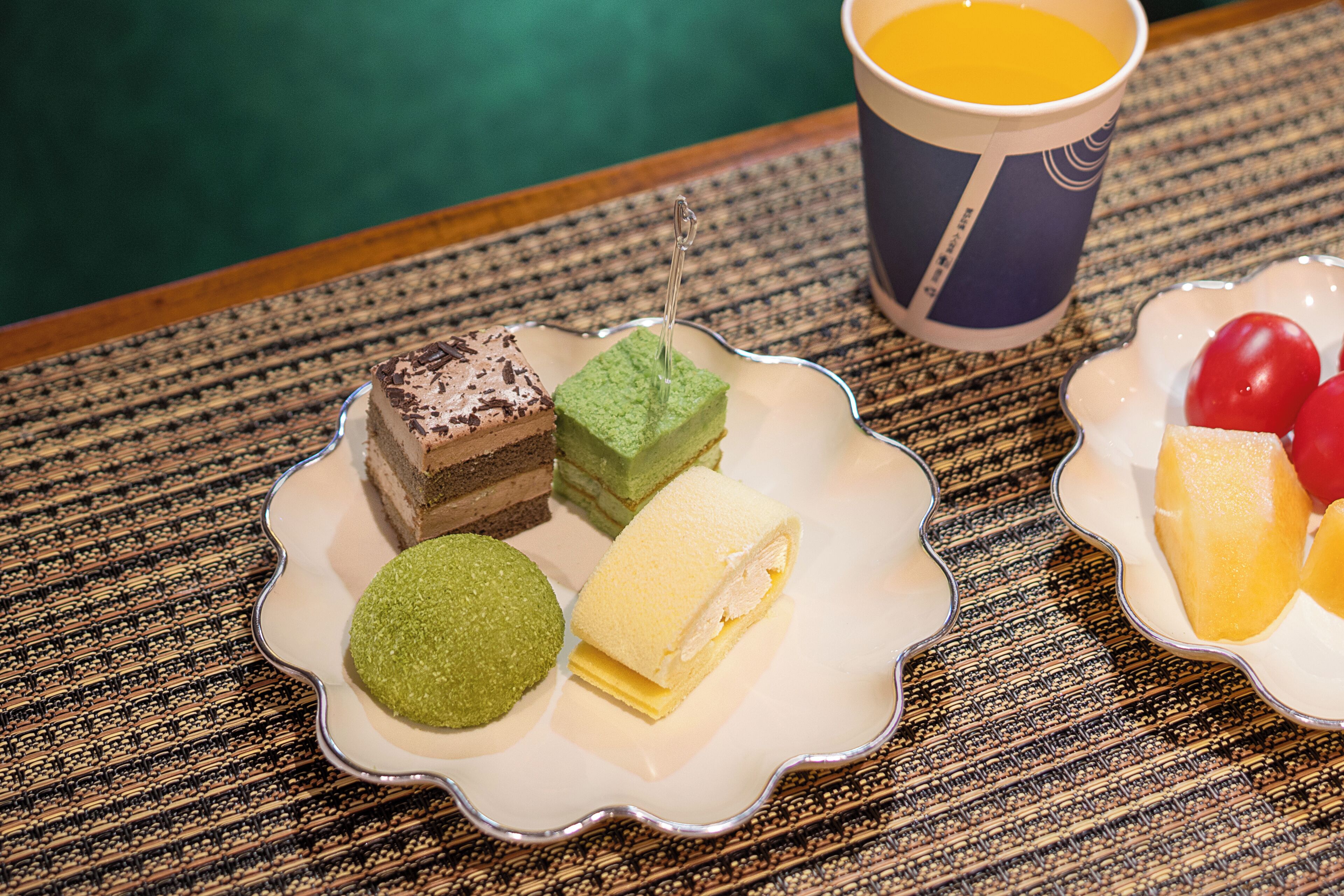 Uma mesa com uma travessa de sobremesas e um copo de sumo de laranja.
