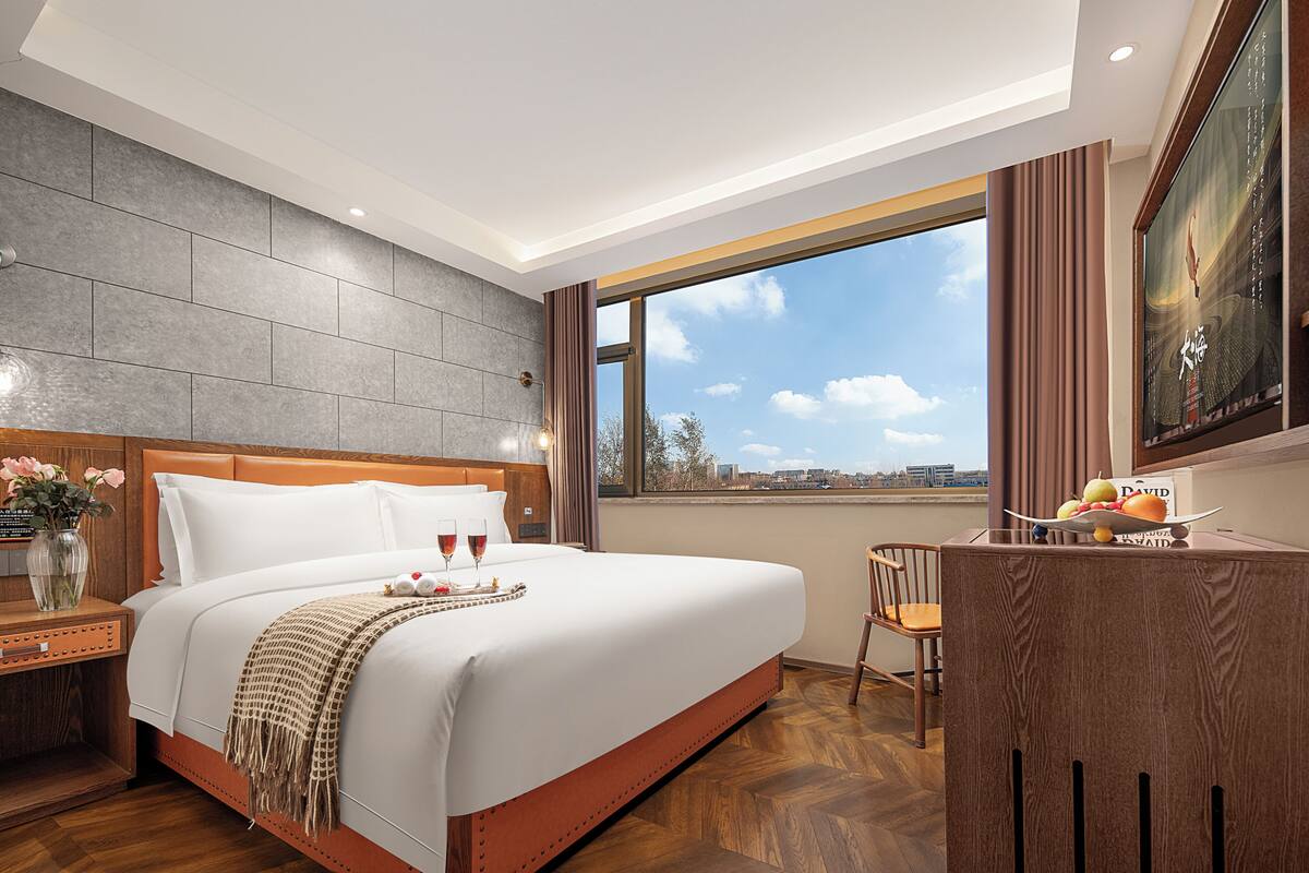 Habitación de hotel con una cama grande, un escritorio, una silla y vistas a la ciudad.