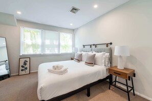 A bedroom with a bed, bedside table, lamp, and a framed picture on the wall. - Hampton Bays Townhouse - Pool, Beach Access (Hampton Bays)