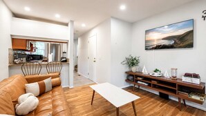 A modern living room with a leather sofa, a white coffee table, and a wooden TV stand with books and decorative items. - Hampton Bays Townhouse - Pool, Beach Access (Hampton Bays)