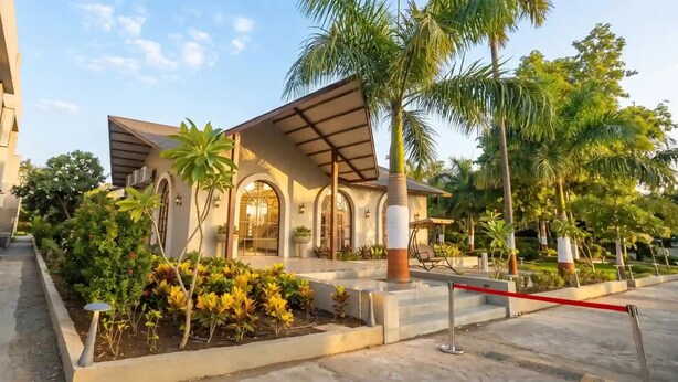 A modern building with arched windows, a covered patio, and a garden with various plants.