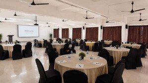 Une salle de conférence équipée de plusieurs tables rondes, de chaises noires et d’un écran de projection affichant le mot « Bienvenue ».