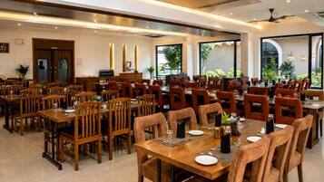 A spacious dining area with multiple tables and chairs, a kitchen area, and large windows providing natural light.