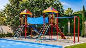 Un parque infantil con dos estructuras de juego, un tobogán azul y columpios rojos.
