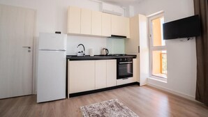 Cocina compacta con refrigerador, estufa, horno y ventana con cortinas.
