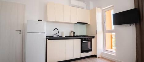 A compact kitchen with a refrigerator, stove, oven, and a window with curtains.