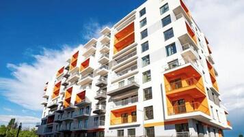 A multi-story residential building with balconies, a clear sky, and a visible street.
