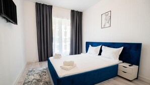 Una habitación de hotel con una cama grande, una mesita de noche, un televisor montado en la pared y una ventana con cortinas.