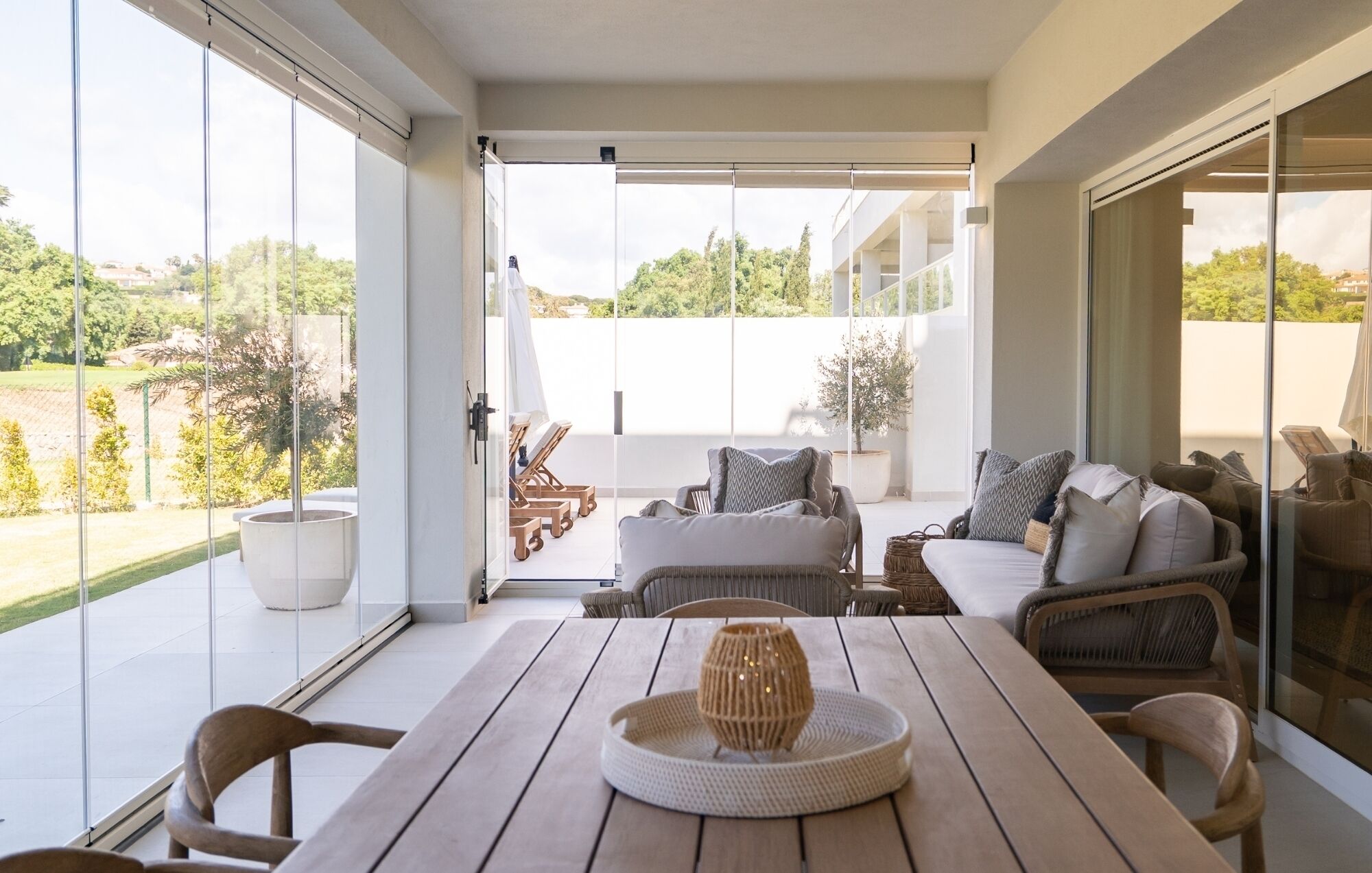 Une vaste terrasse dotée d’une table en bois, de chaises en osier et d’un canapé avec des coussins.