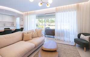 Ein modernes Wohnzimmer mit Sofa, Hocker und einem Essbereich mit Stühlen.