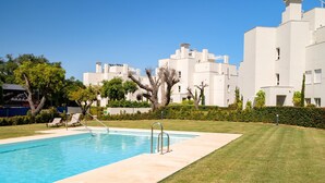 Una piscina con agua cristalina azul, rodeada de un césped cuidado y una hilera de edificios blancos modernos.