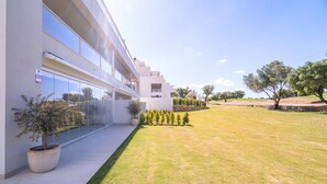 Un edificio moderno con fachada de vidrio, un camino pavimentado y un área ajardinada con árboles.