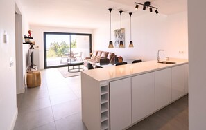 A modern kitchen with a central island, dining area with a table and chairs, and a living room with a sofa. - Exclusive Two-Bed Coastal Apartment in Pure South (Manilva)