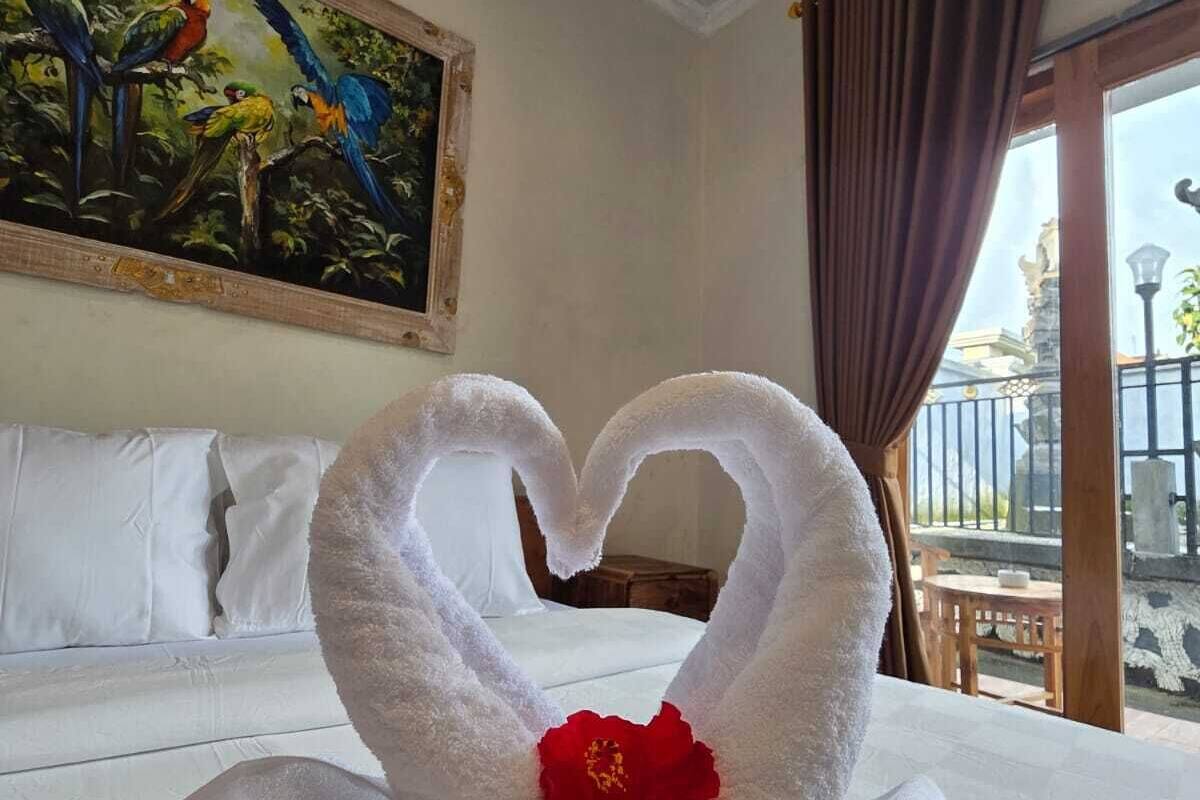A hotel room with a bed, a painting on the wall, and a heart-shaped towel decoration.