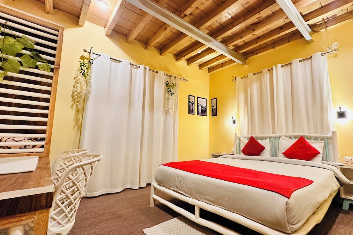 A bedroom with a bed, white curtains, a wooden ceiling, a bedside table, and a nightstand.