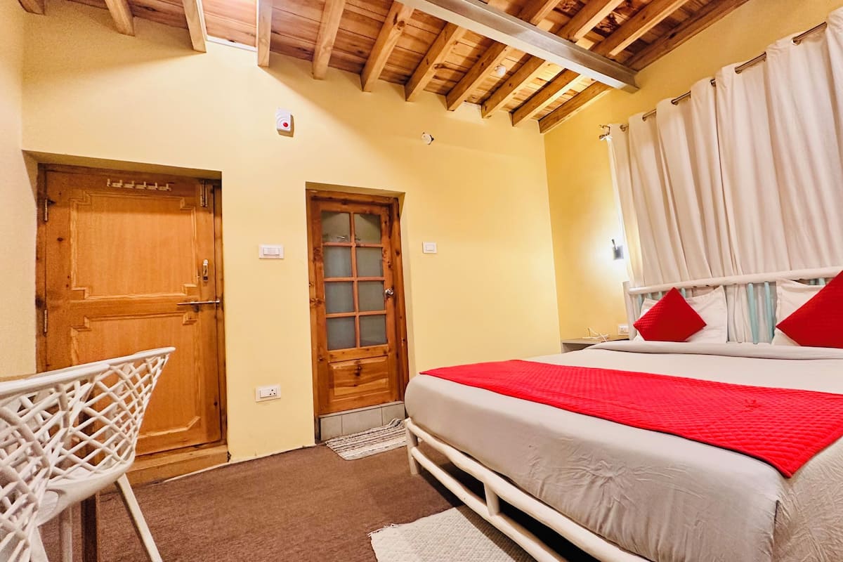 A bedroom with a bed, a wooden door, a white chair, and a window with curtains.