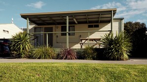 A single-story house with a covered porch, a car parked in front, and various plants around.