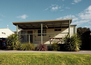 A single-story house with a covered porch, a car parked in front, and various plants around.