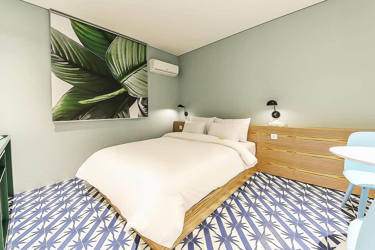 Une chambre à coucher avec un lit, des lampes de chevet, un climatiseur fixé au mur et une grande plante.