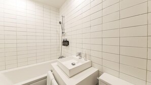 Moderni kylpyhuone, jossa on valkoiset laatat, kylpyamme, peilillä varustettu pesuallas ja wc.