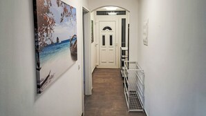 Käytävässä on taulu, jossa on kuvattuna merimaisema, valkoinen ovi ja metallinen hylly.